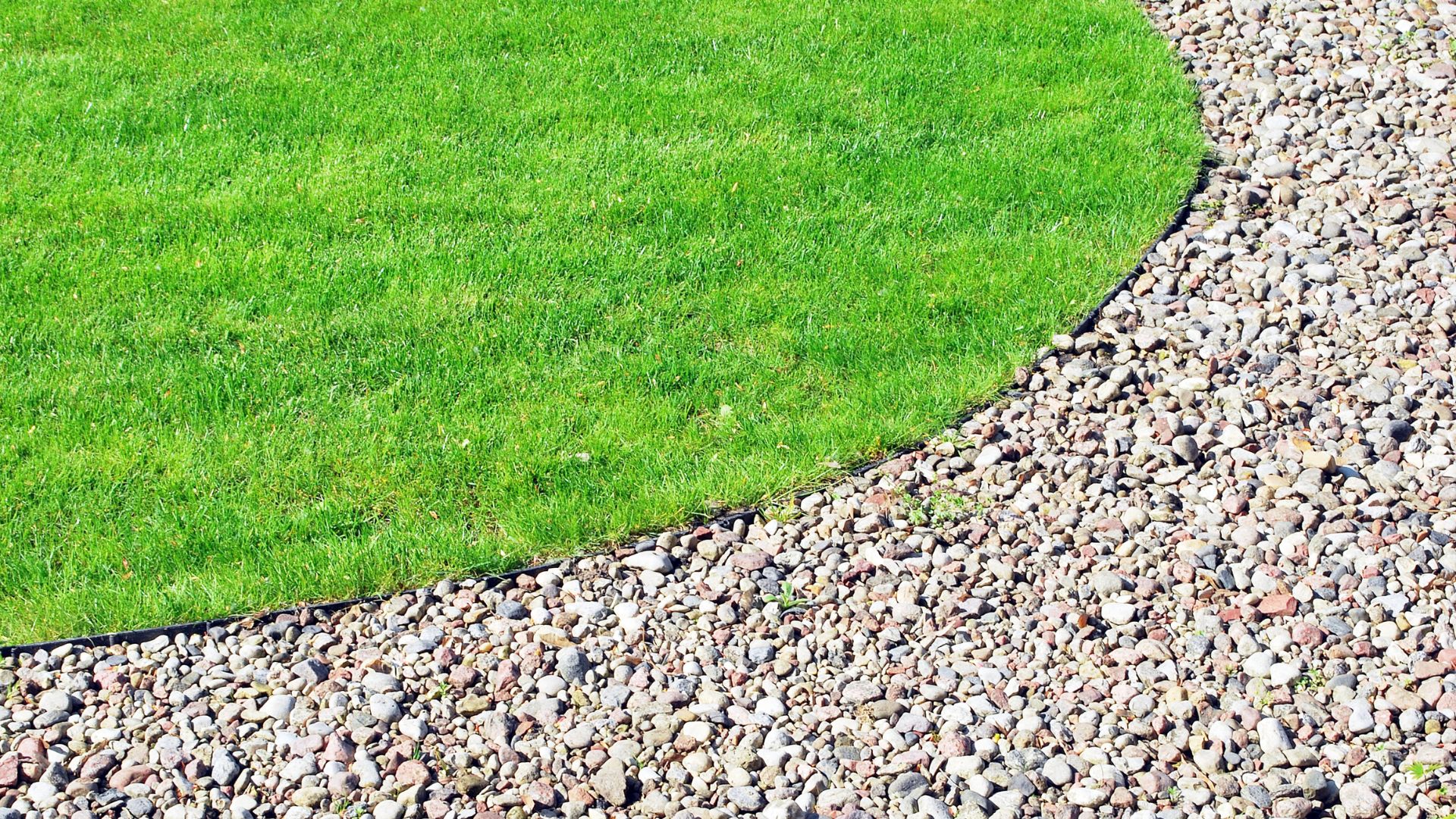 Green lawn with curved edge bordered by multicolored stone gravel path