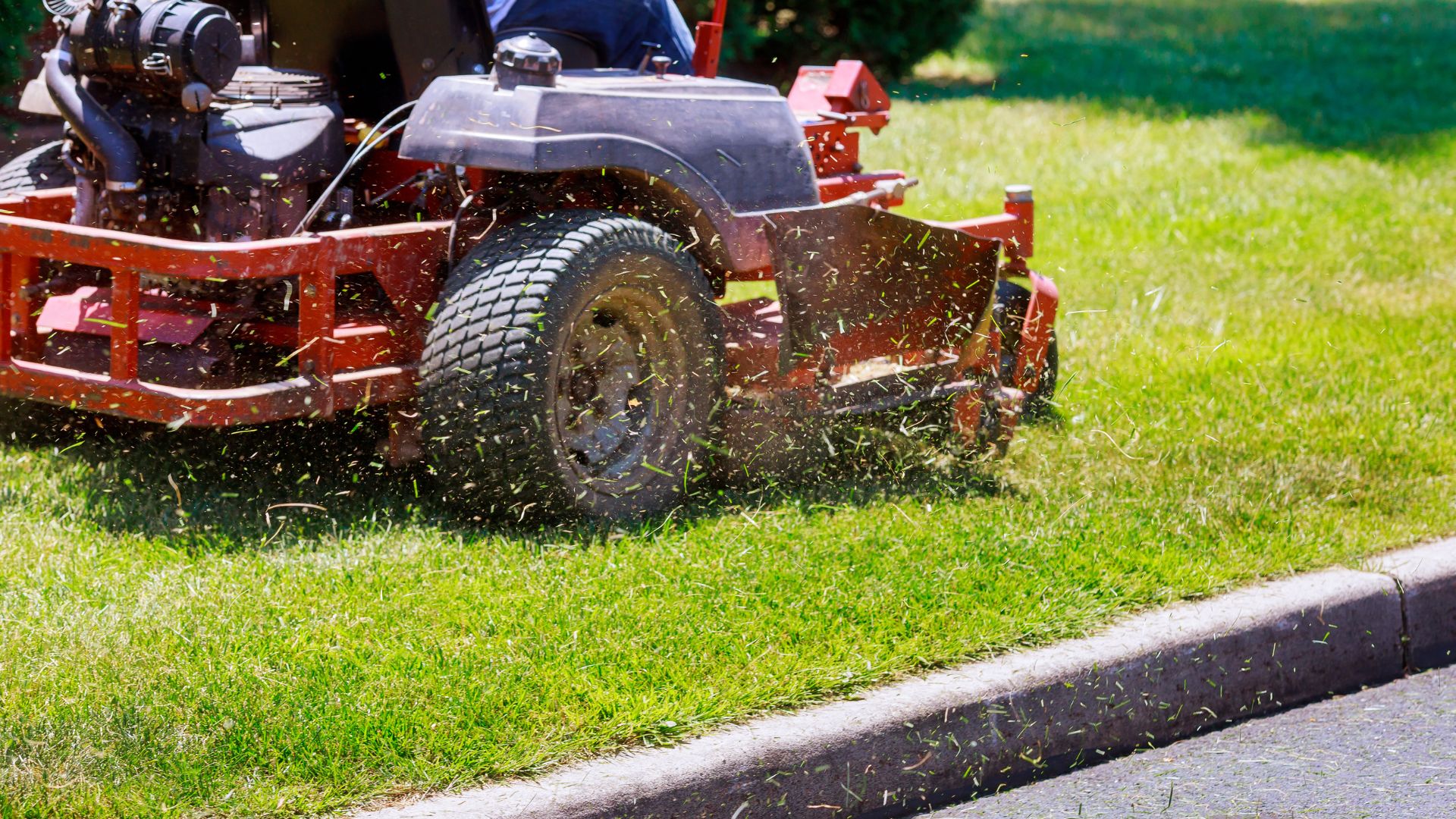 Red zero-turn lawn mower cutting grass with grass clippings flying